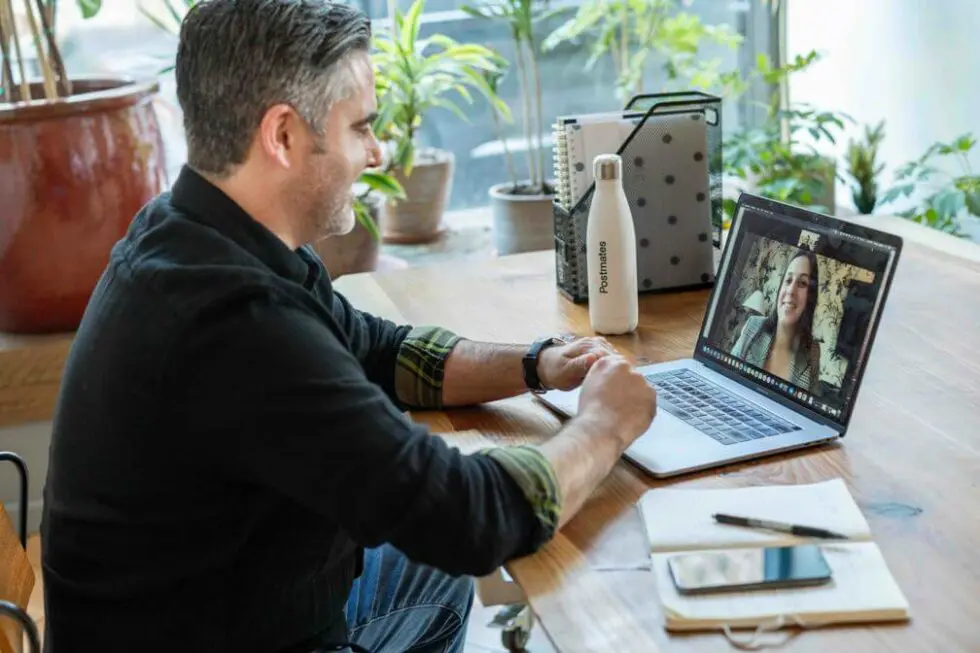 A person sitting at a desk using a laptop, surrounded by plants and pottery, focused on their work.