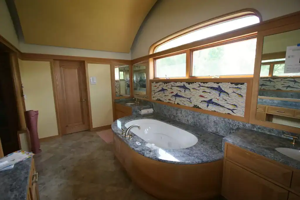 Mosaic fish wall art in a bathroom with a curved window and wooden accents.