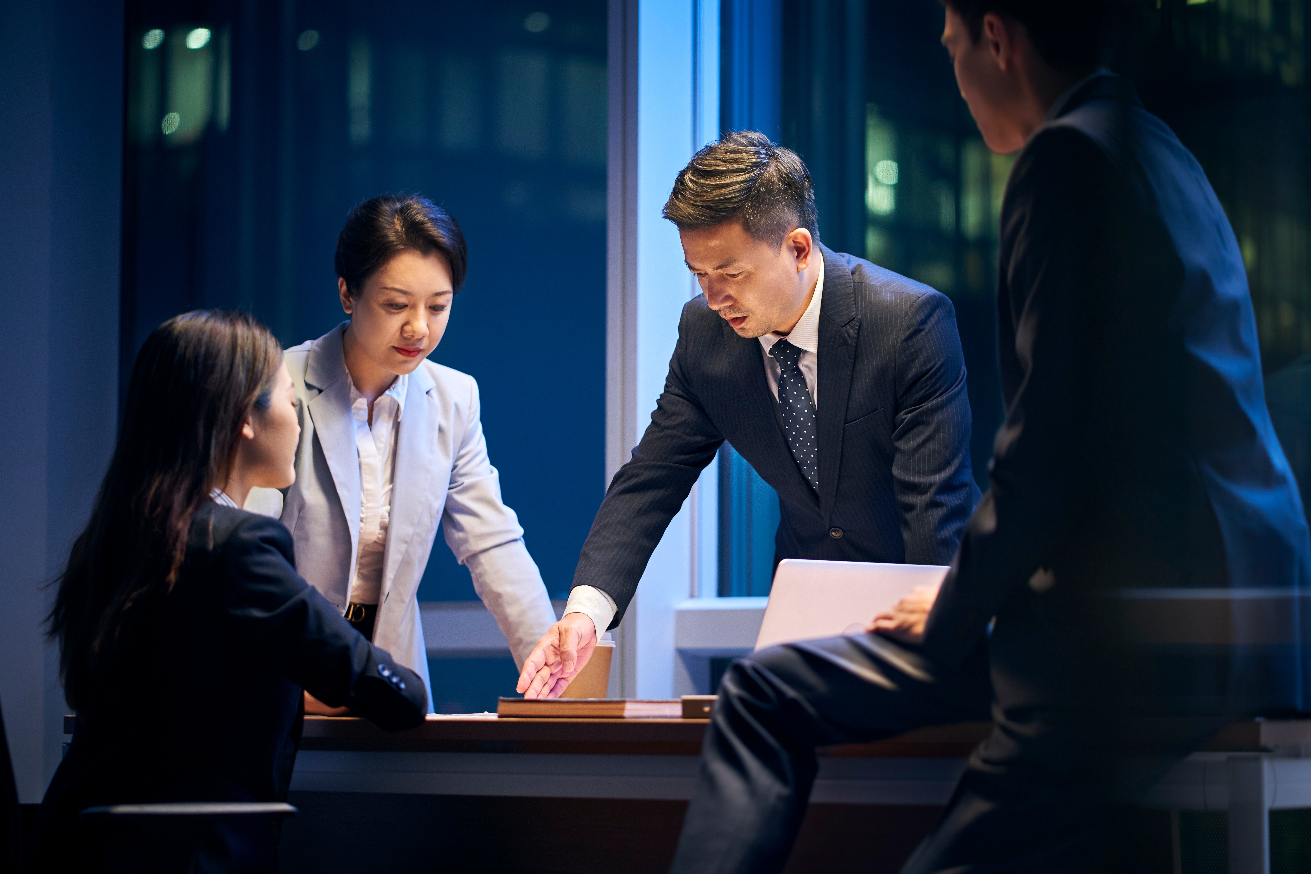 Small group of professionals gathered around a table, collaboratively reviewing documents and discussing options, representing structured decision-making and analytical evaluation in a business setting.