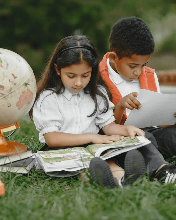 Children are sitting on the grass, reading a book together
