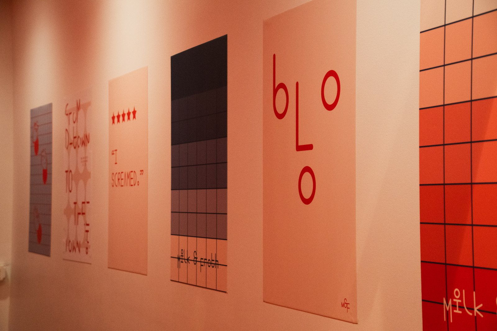 Series of red and pink typographic posters hung along a gallery wall