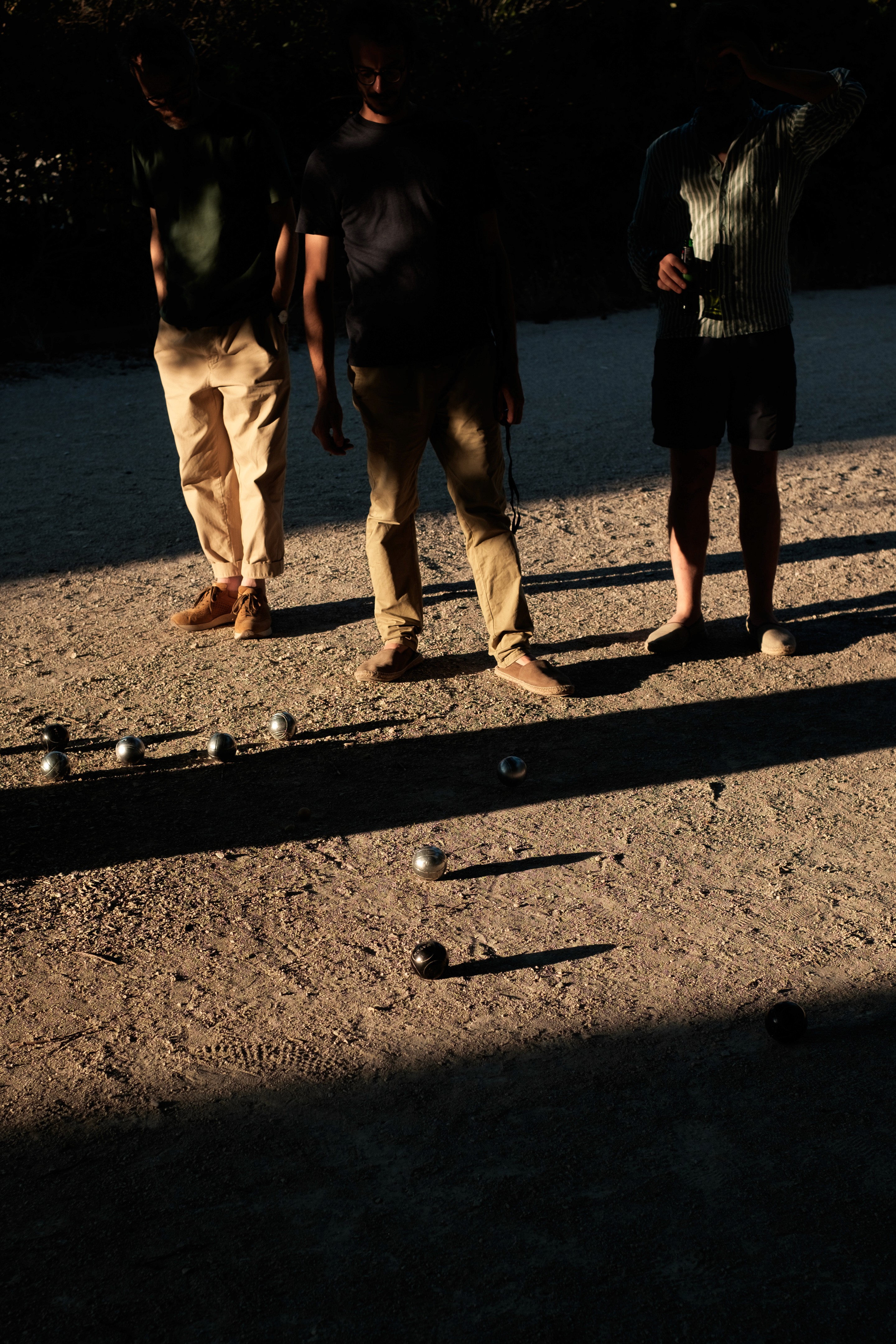 Three people play boules as the sun sets