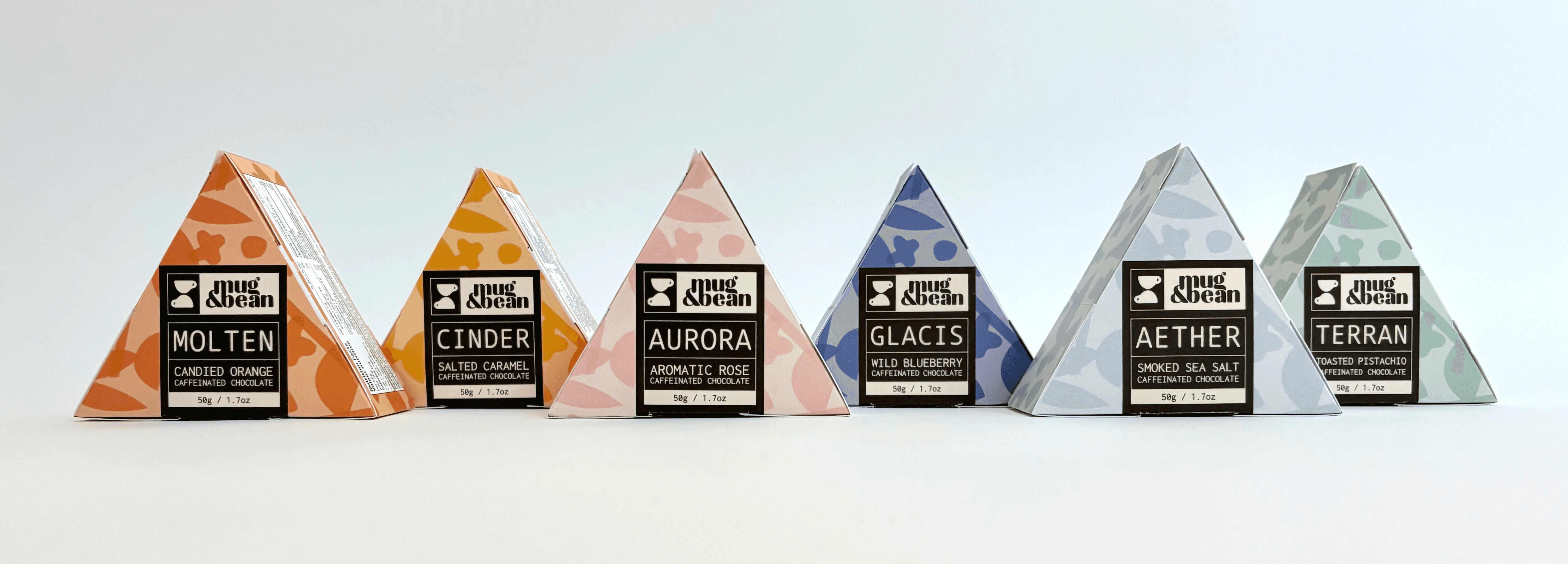 Gemini said A row of six triangular prism-shaped product boxes for Mug & Bean caffeinated chocolate, each featuring a different color and pattern theme including orange for "Molten," yellow for "Cinder," pink for "Aurora," dark blue for "Glacis," light blue for "Aether," and sage green for "Terran."