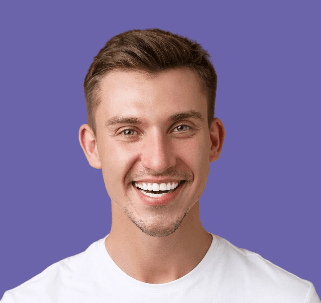 A person with long, curly hair and red lipstick stands in front of a brick wall, looking directly at the camera with a neutral expression.