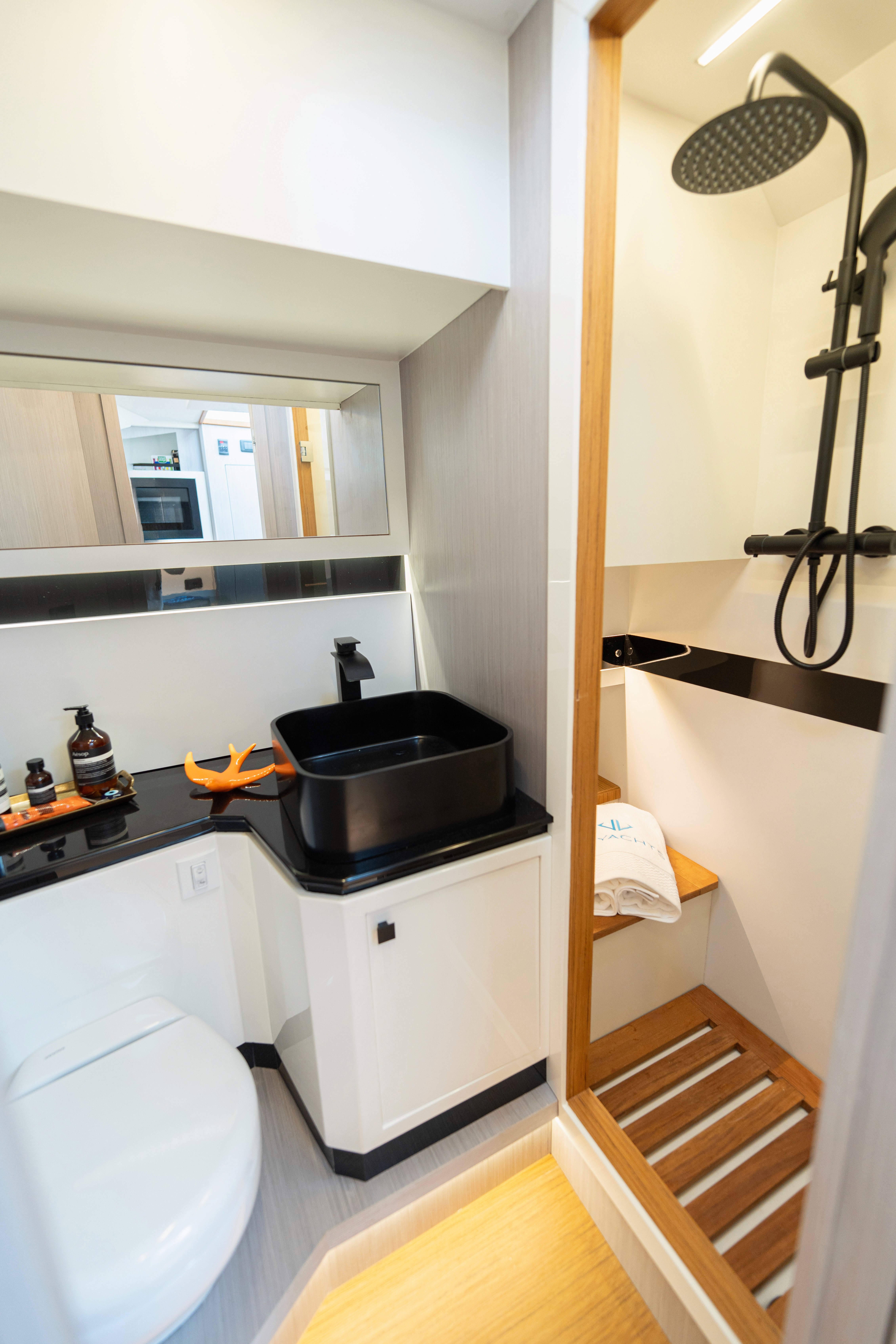 Une salle de bain moderne et compacte comprend des toilettes blanches élégantes, un comptoir noir avec un lavabo et une serviette orange vif suspendue à côté.