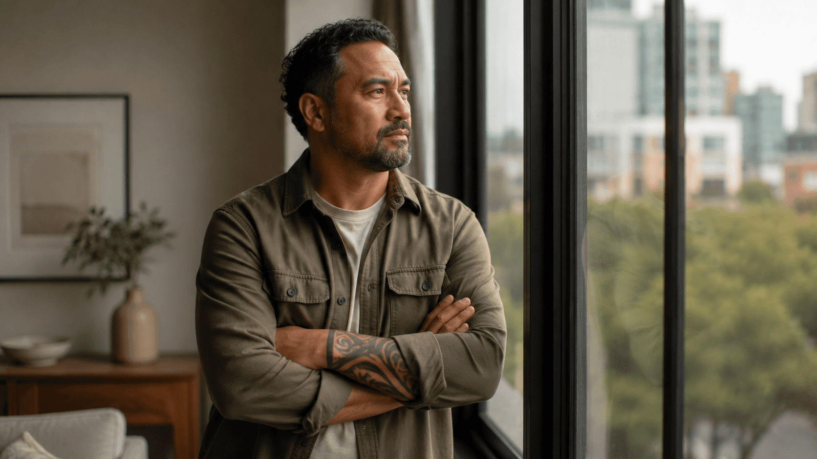 Man standing by a large window in a softly lit modern apartment