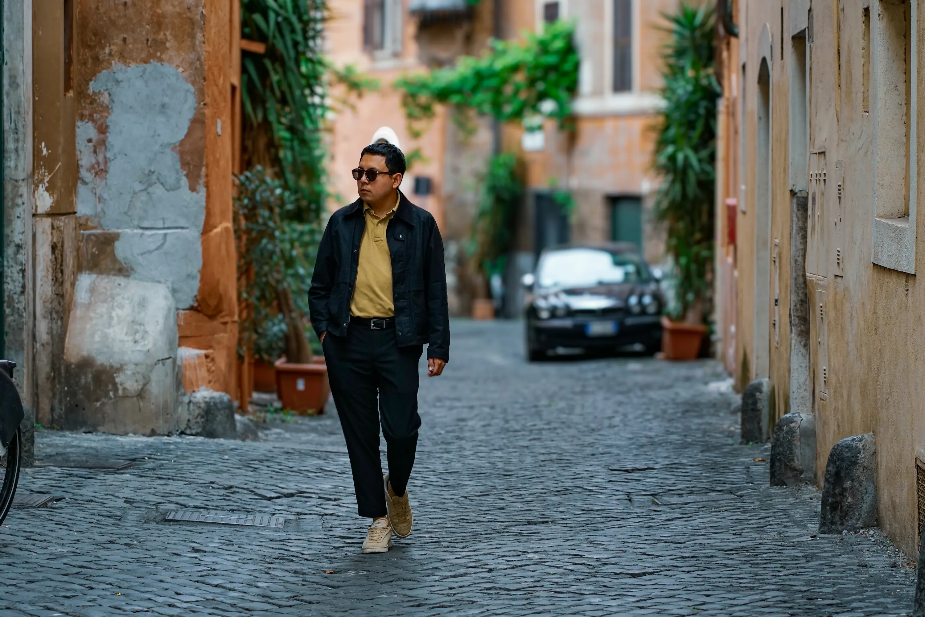 Homme marchant dans une rue pavée de Rome, entourée de façades anciennes et de végétation.