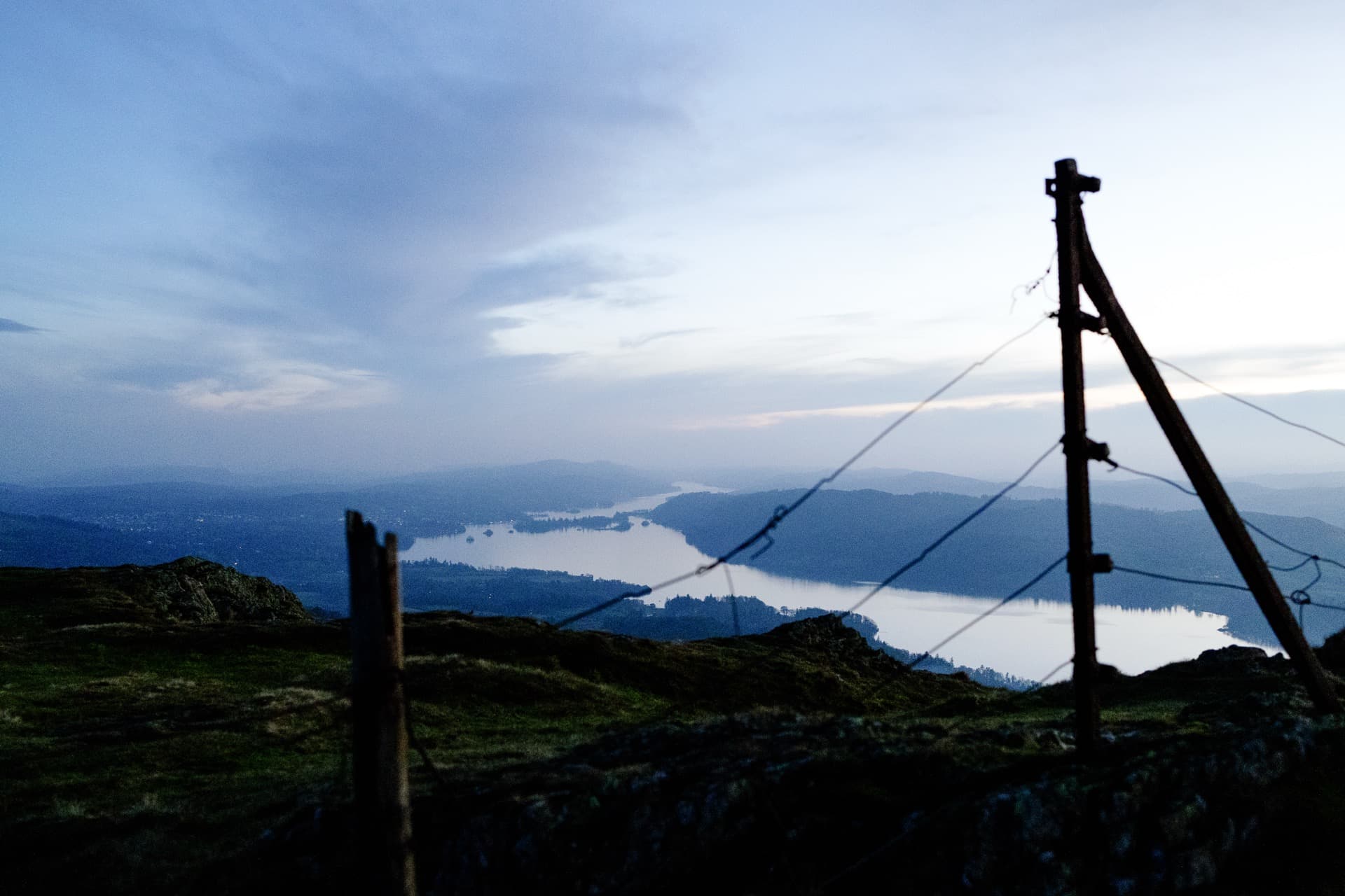 Silhouetted fence posts with wire against twilight sky, Windermere lake reflecting light between wooded islands below Wansfell summit