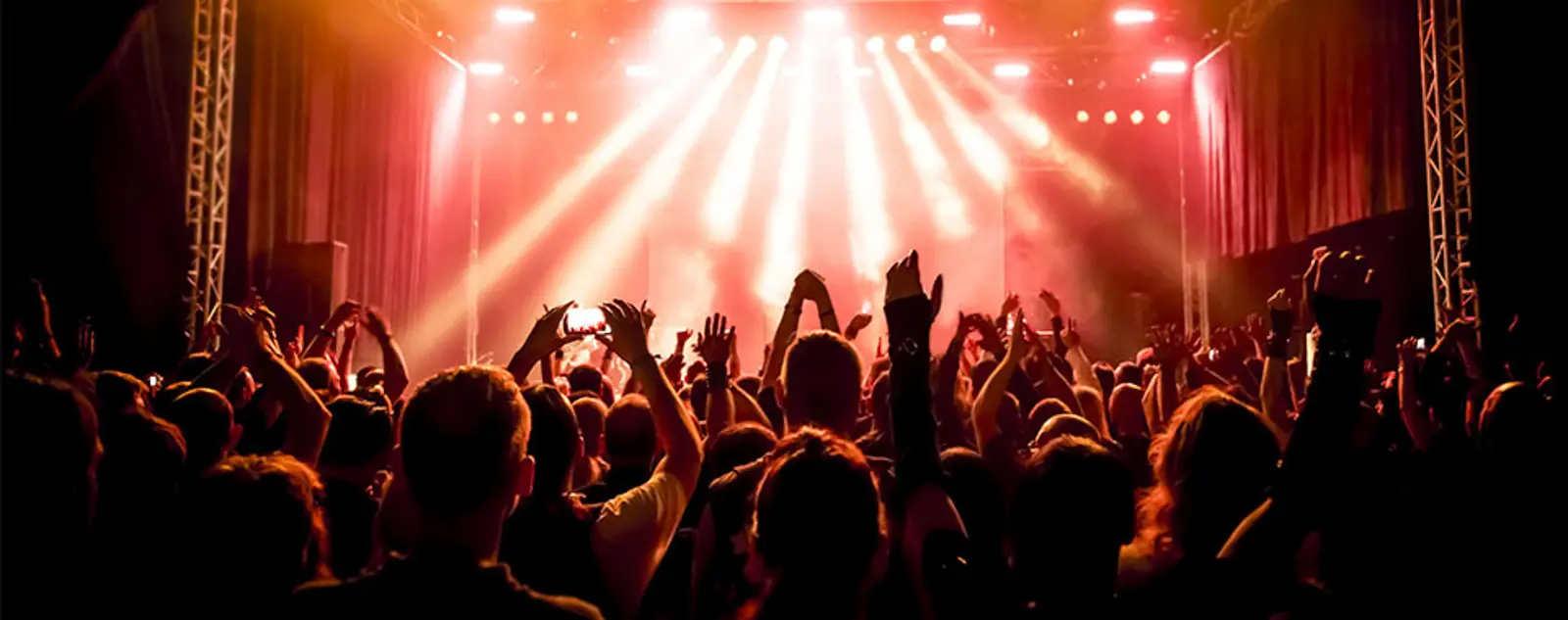 Concert crowd with hands raised towards bright stage lights.