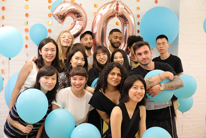 A photo of a group of students surrounded by blue balloons and in the background the number twenty made also from shiny balloons.