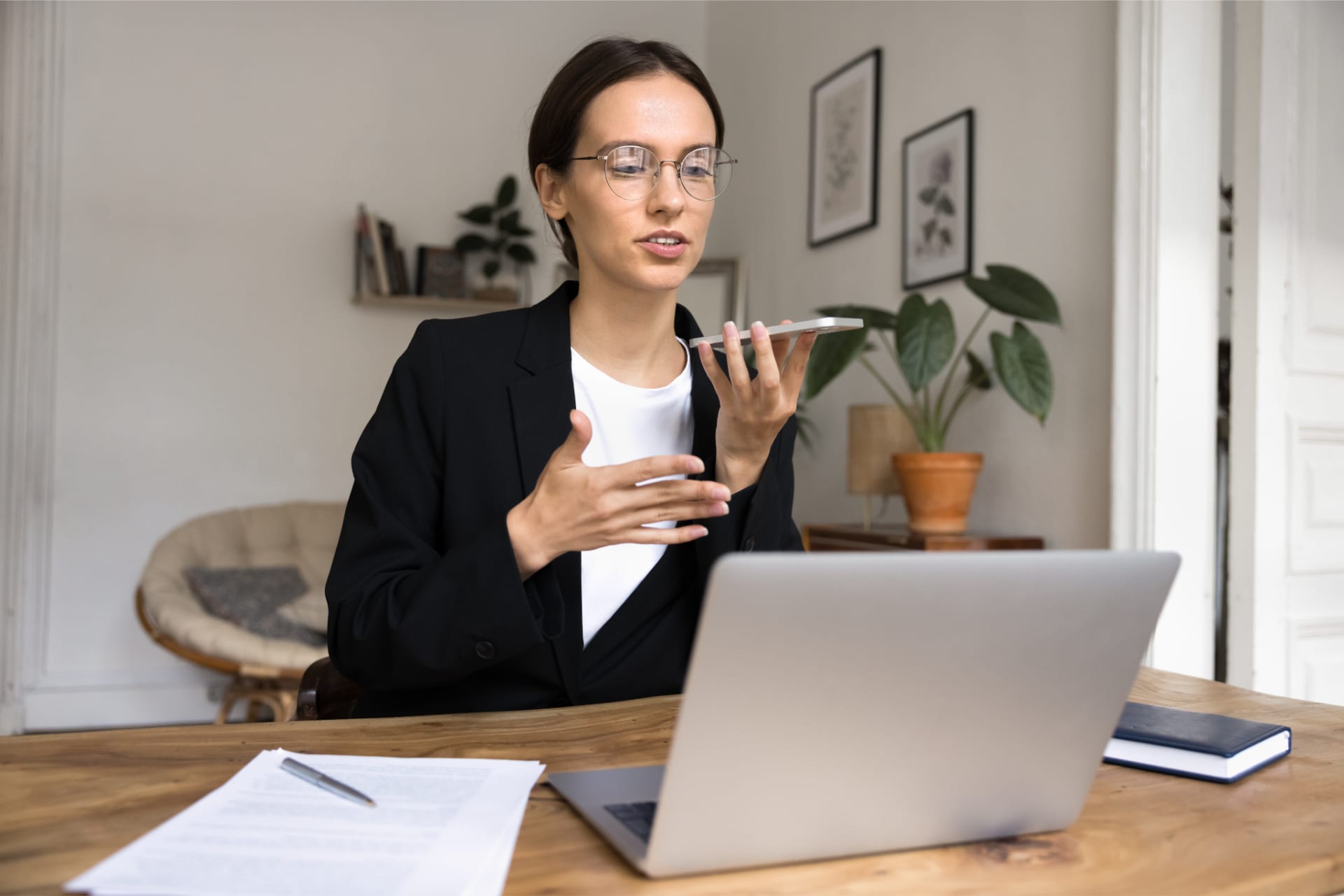 Young businesswoman hold smartphone using speaker function lead formal conversation at workplace with laptop