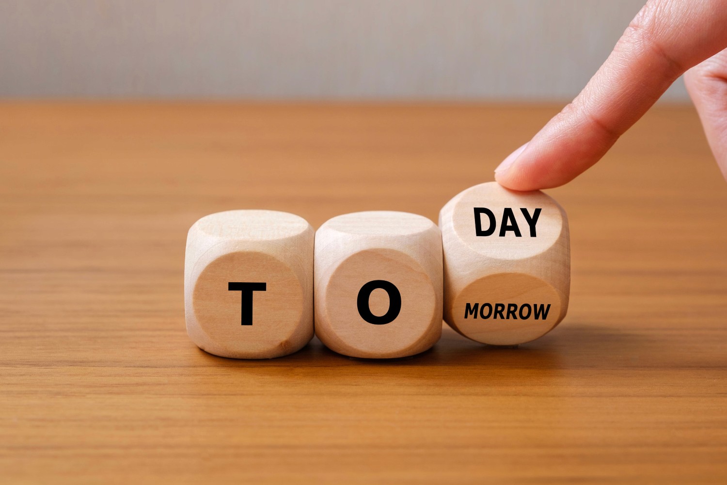 Hand turning wooden blocks from 'tomorrow' to 'today' to represent overcoming procrastination