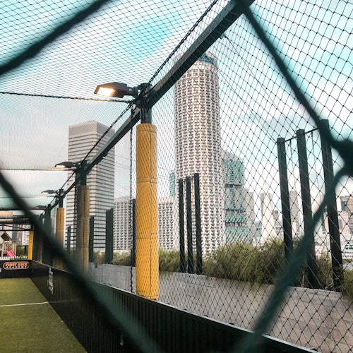Elevated football field with netting, framed by tall buildings and skyscrapers in an urban setting.