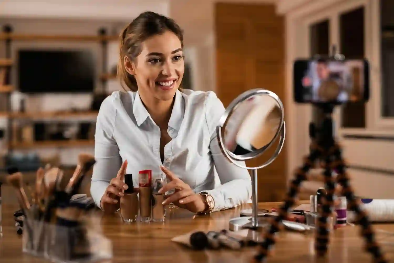 Beauty blogger presenting various foundation bottles and makeup products while recording a video tutorial on her smartphone.