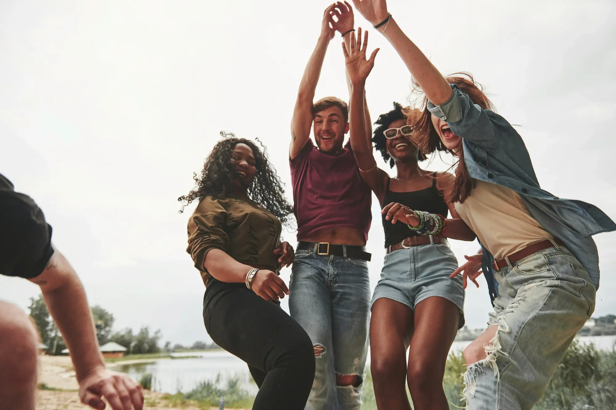 Diverse group of friends joyfully jumping outdoors by a lake, expressing connection, community, and celebration.