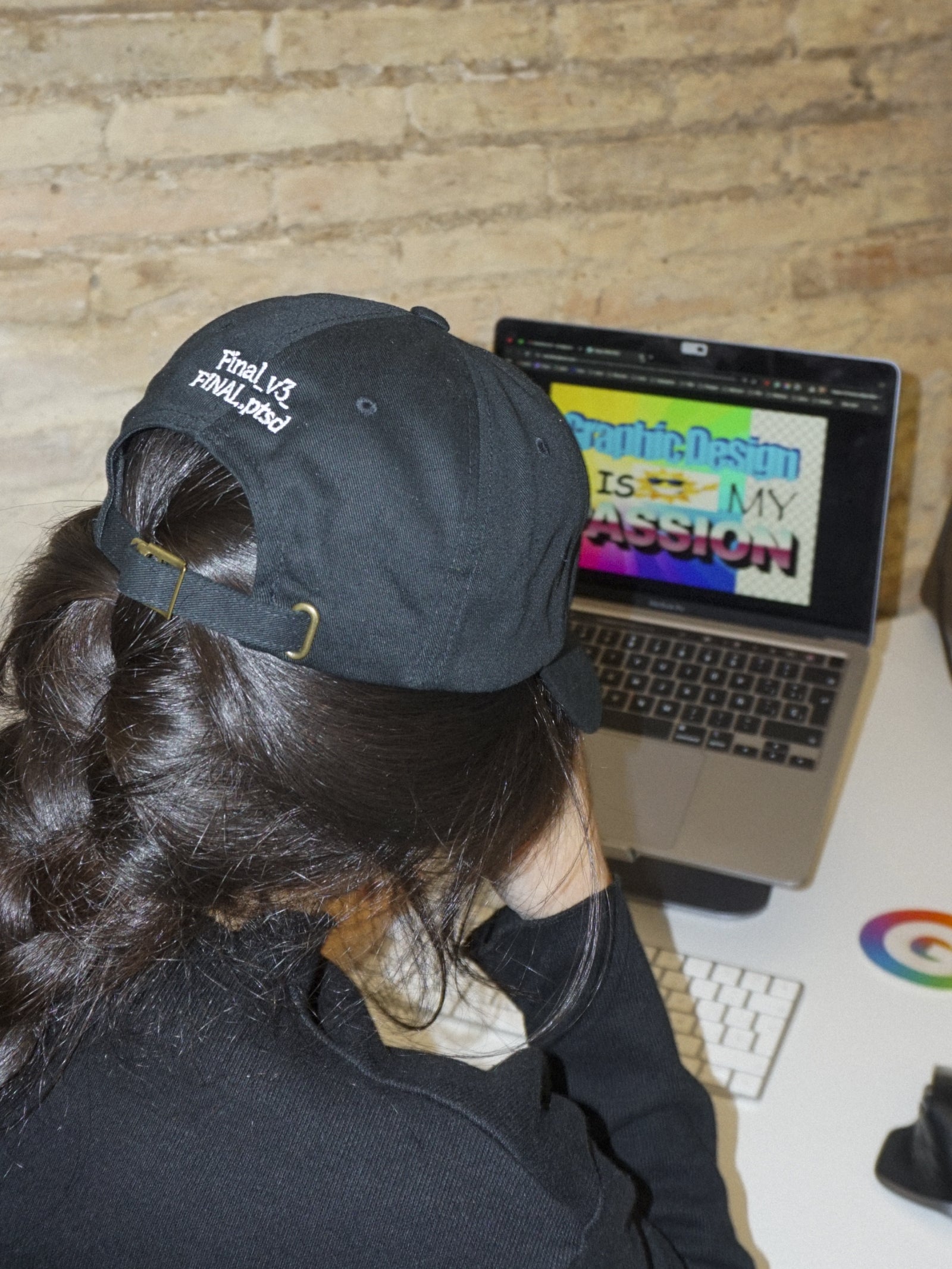 Person wearing a black cap with text, sitting in front of a laptop.