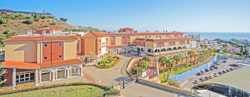 Residential complex aerial view with terracotta and orange colored buildings, curved pathways, blue sky, and surrounding landscaping