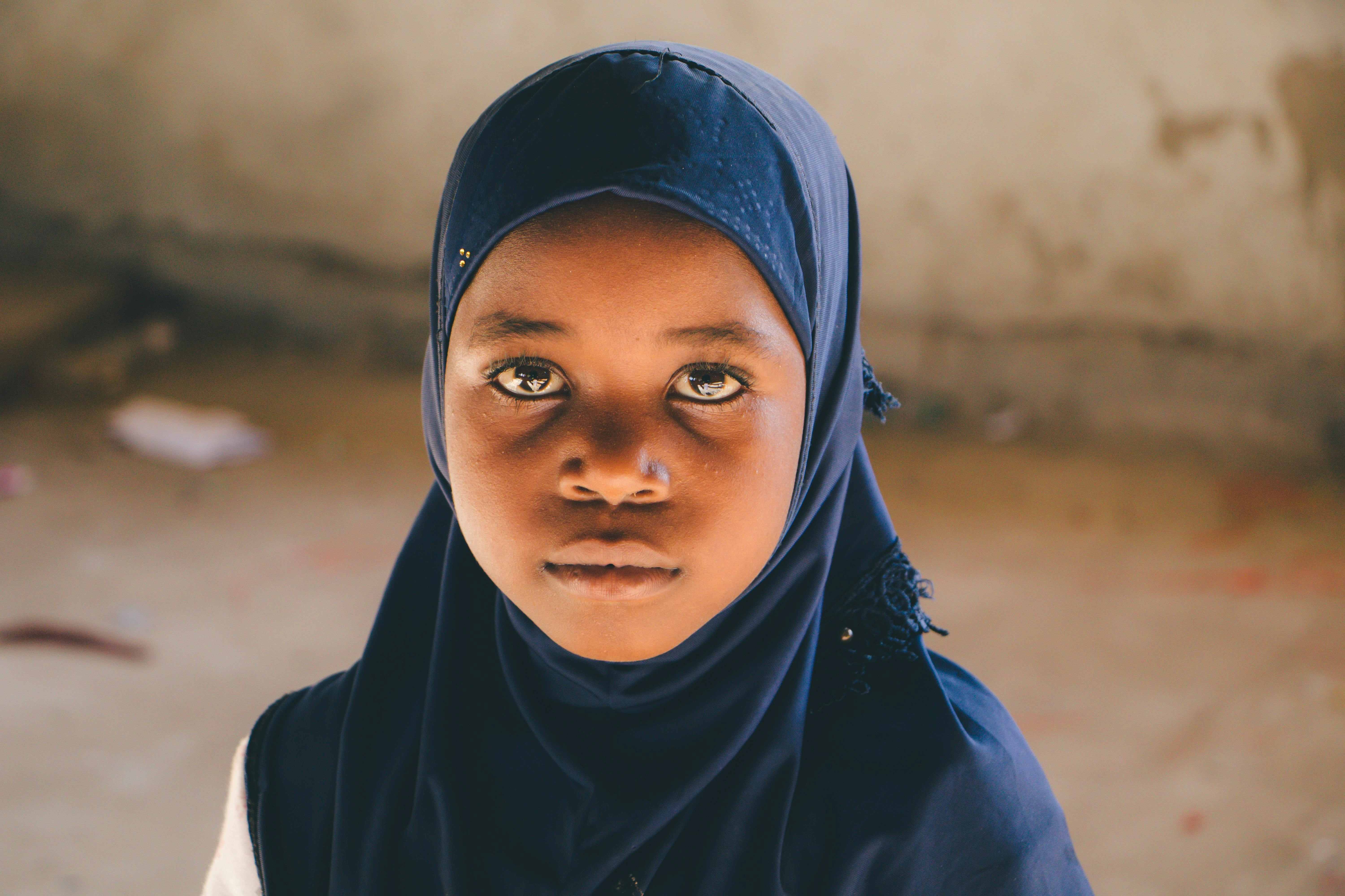 Young girl in a navy headscarf looks directly at the camera with a calm, serious expression.