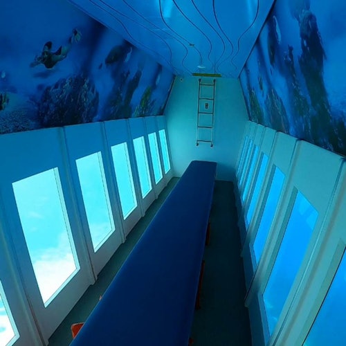 A narrow room with large windows on both sides, blue seating in the center, and underwater-themed decorations on the ceiling and walls.