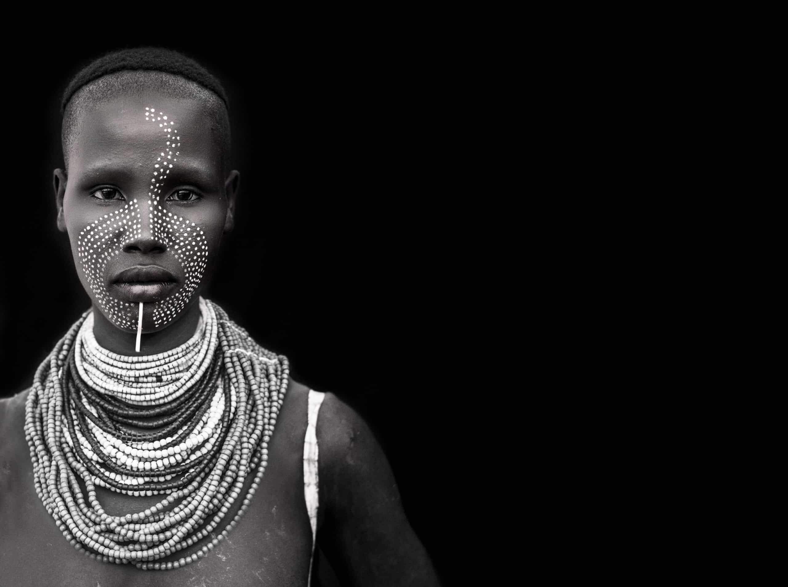 Black-and-white portrait of an Ethiopian woman with luminous skin and tiny dots painted on her face, resembling stars in a constellation.