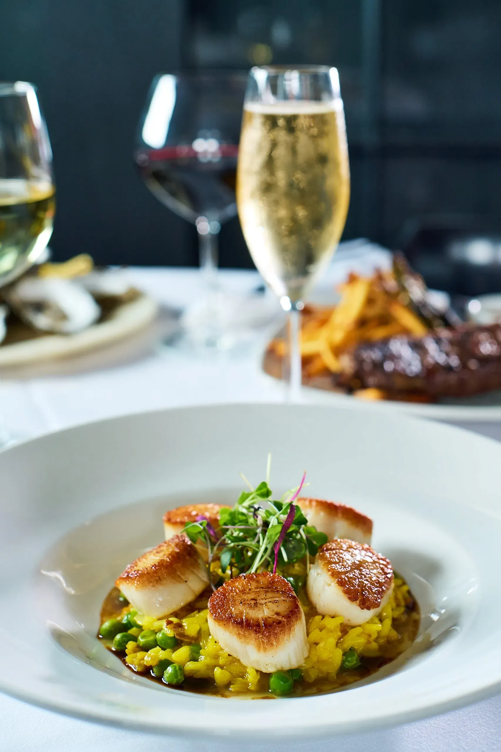 Seared scallops served over green pea risotto with microgreens on a white plate.