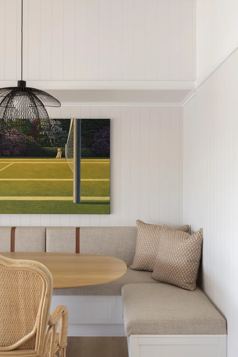 Built-in dining nook with upholstered bench seating and artwork on panelled wall.