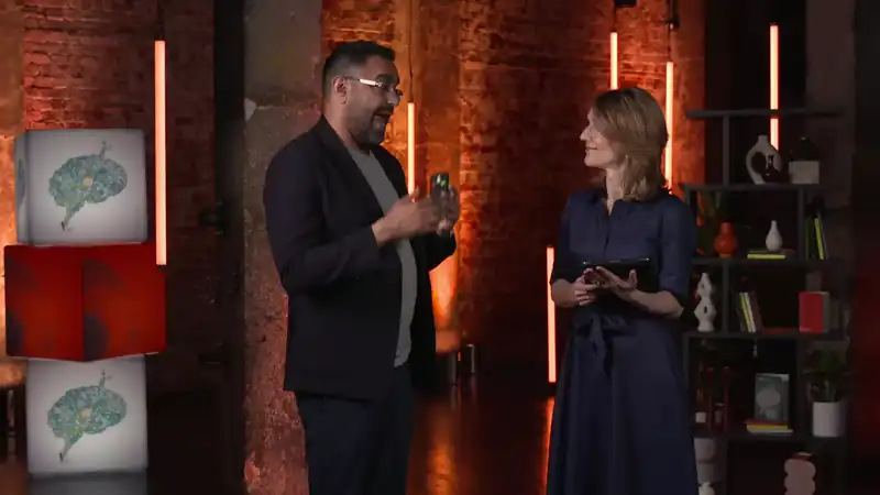 Host and guest in conversation on a studio set, standing under warm vertical lighting elements