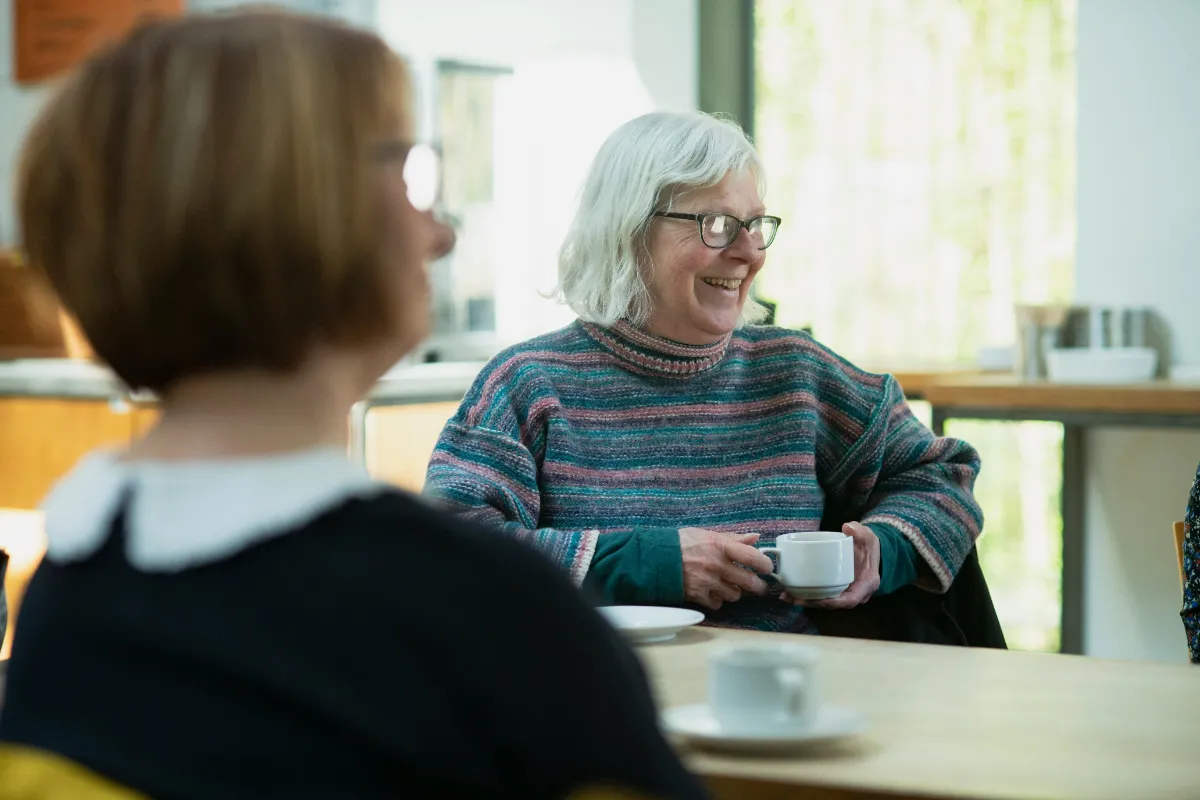A group coordinator smiling while a participant reads a book