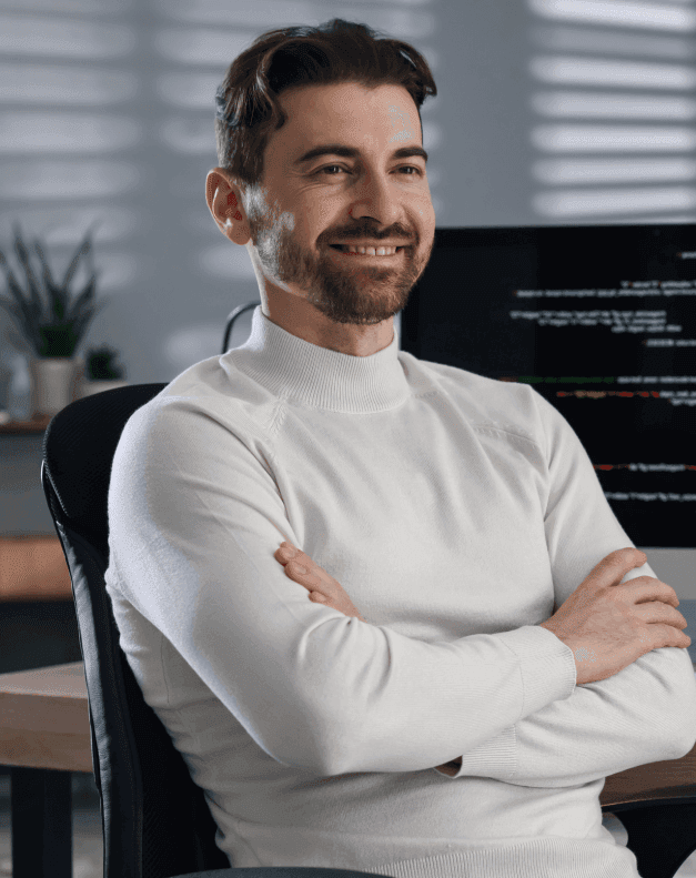 Young person with short, tousled blonde hair wearing an oversized, vibrant orange turtleneck sweater against a soft grey background, conveying a cool, modern look.