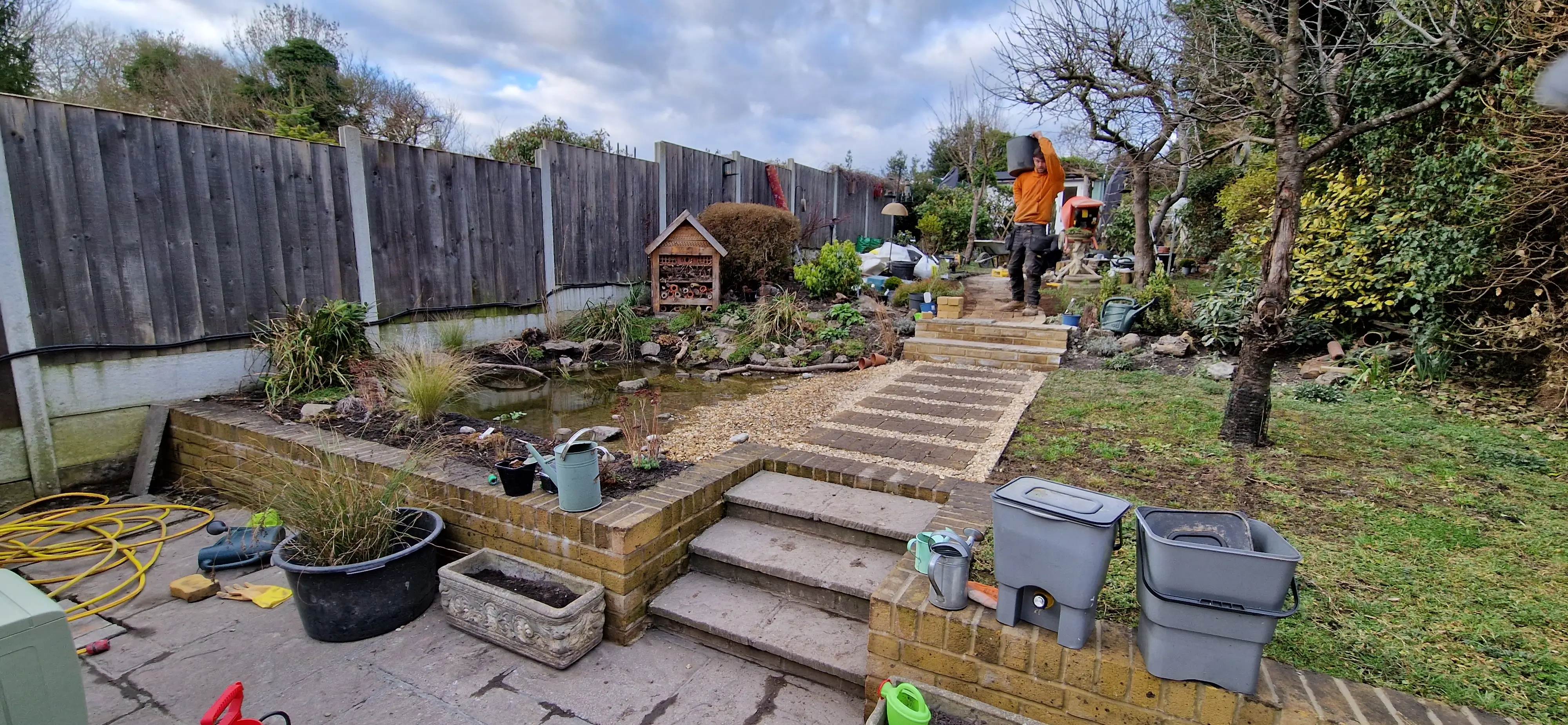 A landscaped garden path with steps, bordered by greenery and colorful plants under a partly cloudy sky.