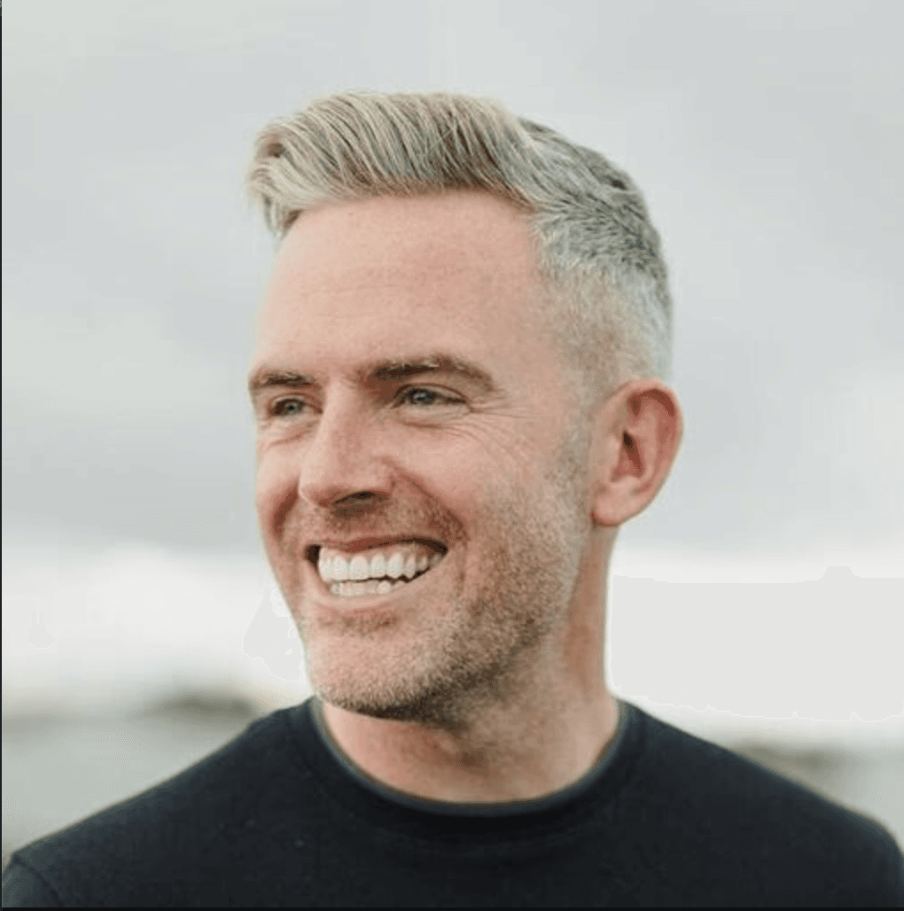 A woman with short curly hair wearing a black t-shirt looks into the camera.