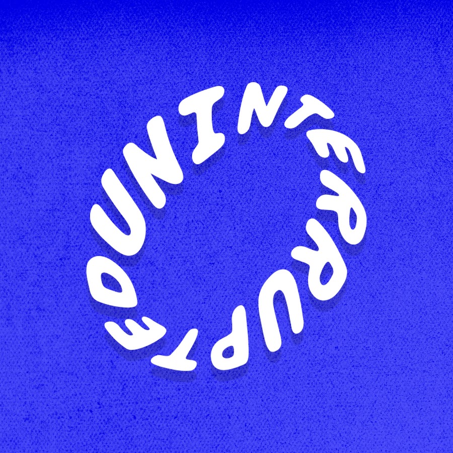 Young person with wavy hair poses confidently in sunlight against a modern building backdrop. Wears a black blazer and silver necklace, conveying elegance.