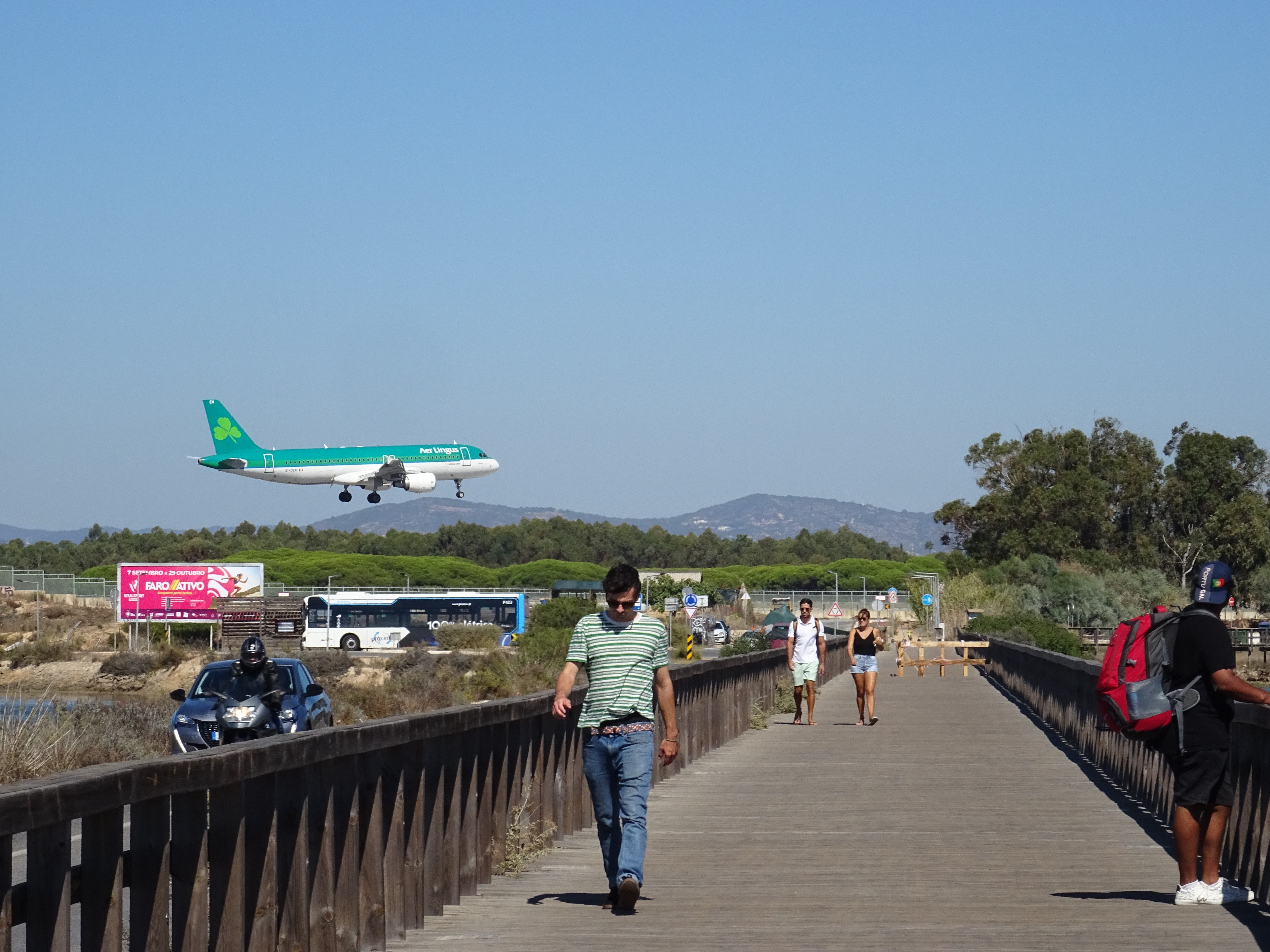 Airplane landing over a walkway with people watching and walking below.