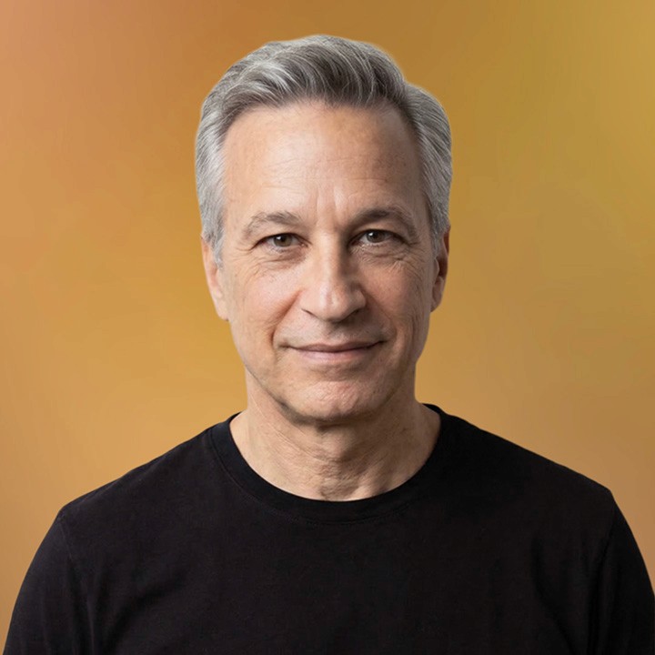 A portrait headshot of a white man with short gray hair wearing a black t shirt, smiling