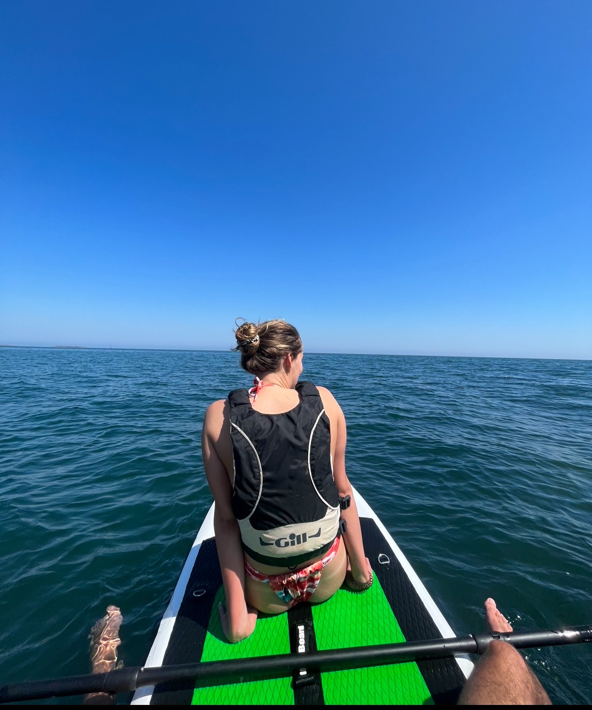 Smiling young woman with curly hair sitting at a laptop, in front of a teal wall.
