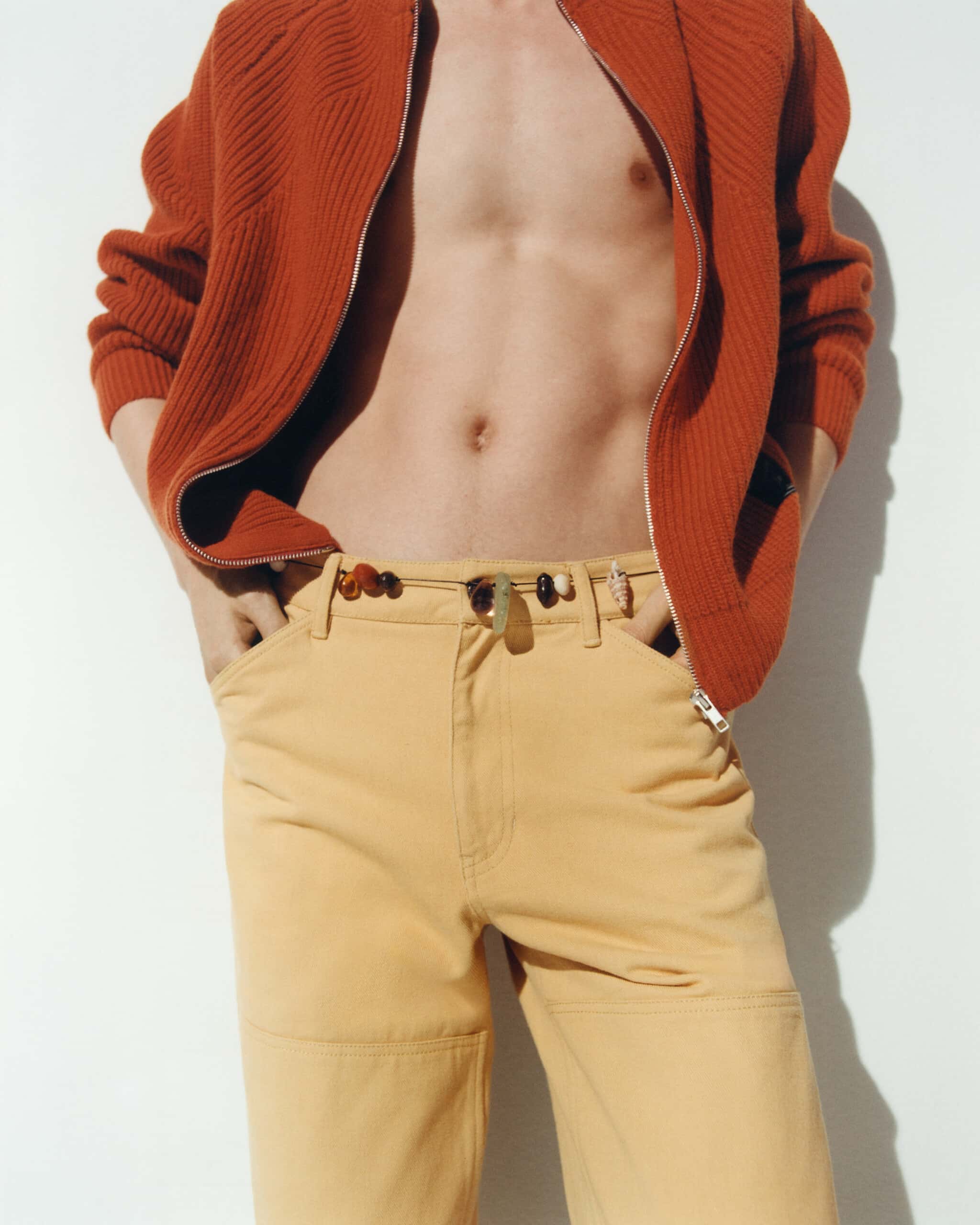 Un homme dont on ne voit pas la tête porte un pull à grosses côtes oranges et un jean jaune