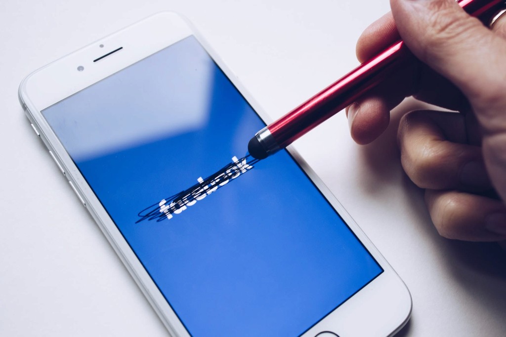 Person using a stylus to cross out the Facebook logo on a smartphone screen.