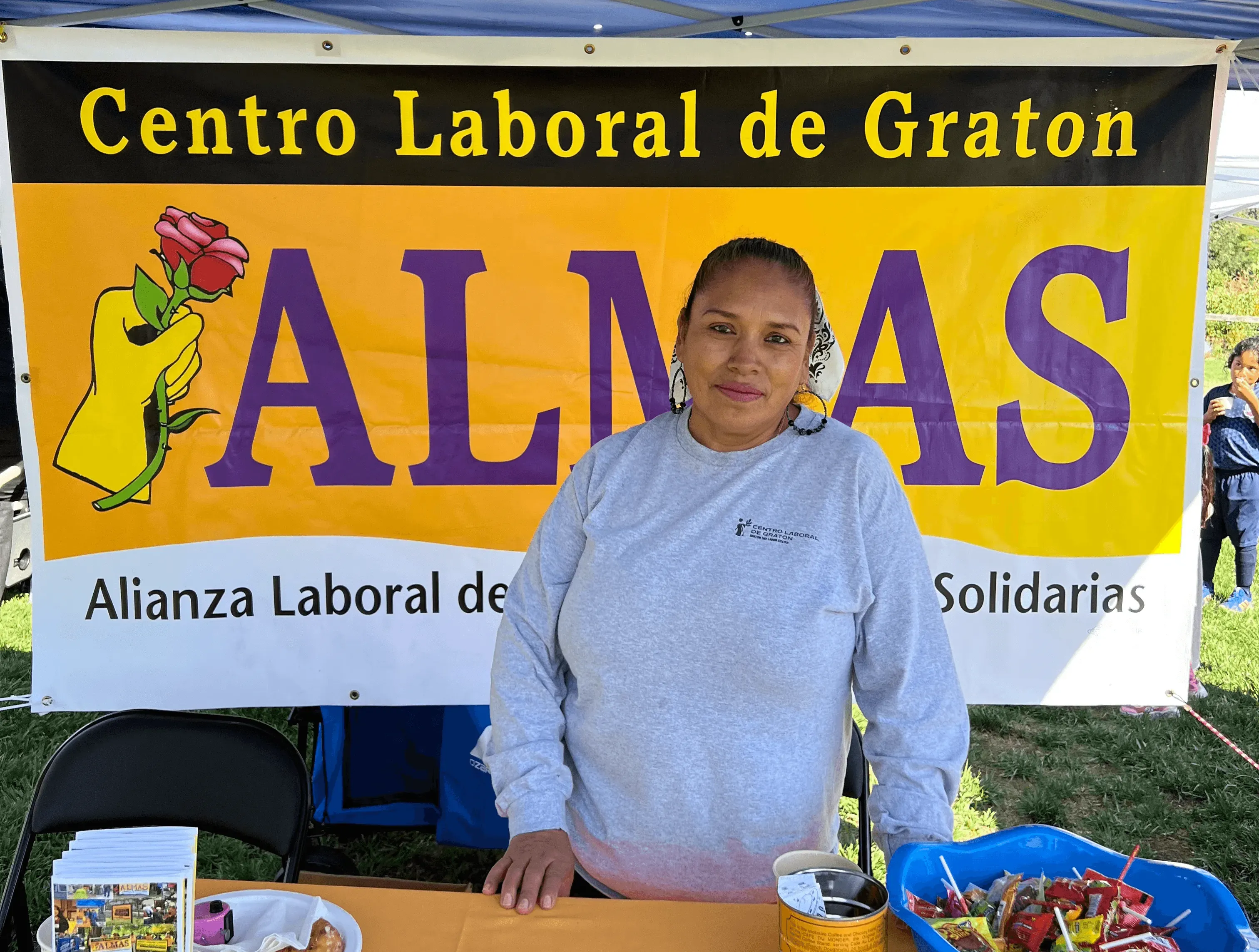A person stands in front of a colorful banner that reads "ALMAS" at an outdoor event.