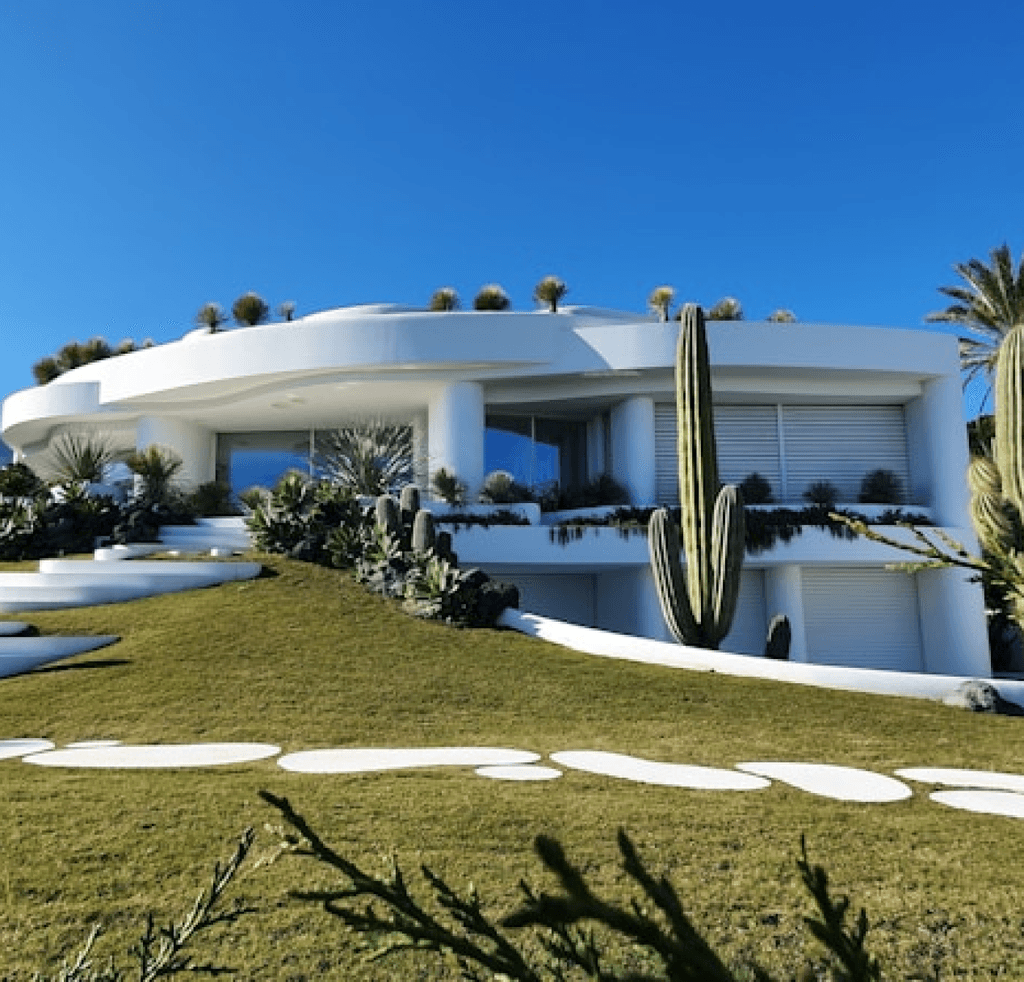 Modern white home with cut lawn and catus in front with spotted stone trail