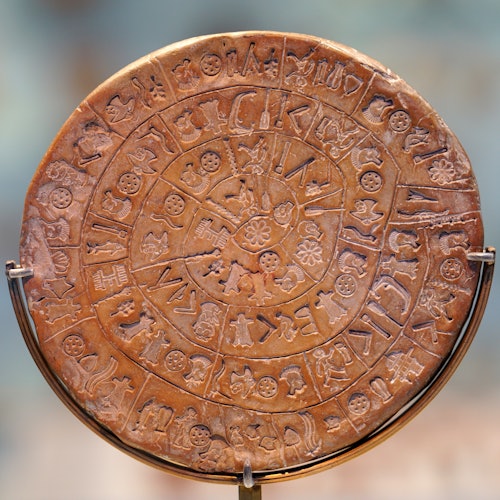 A circular clay disc with intricate symbols and patterns arranged in concentric circles, possibly an ancient artifact.