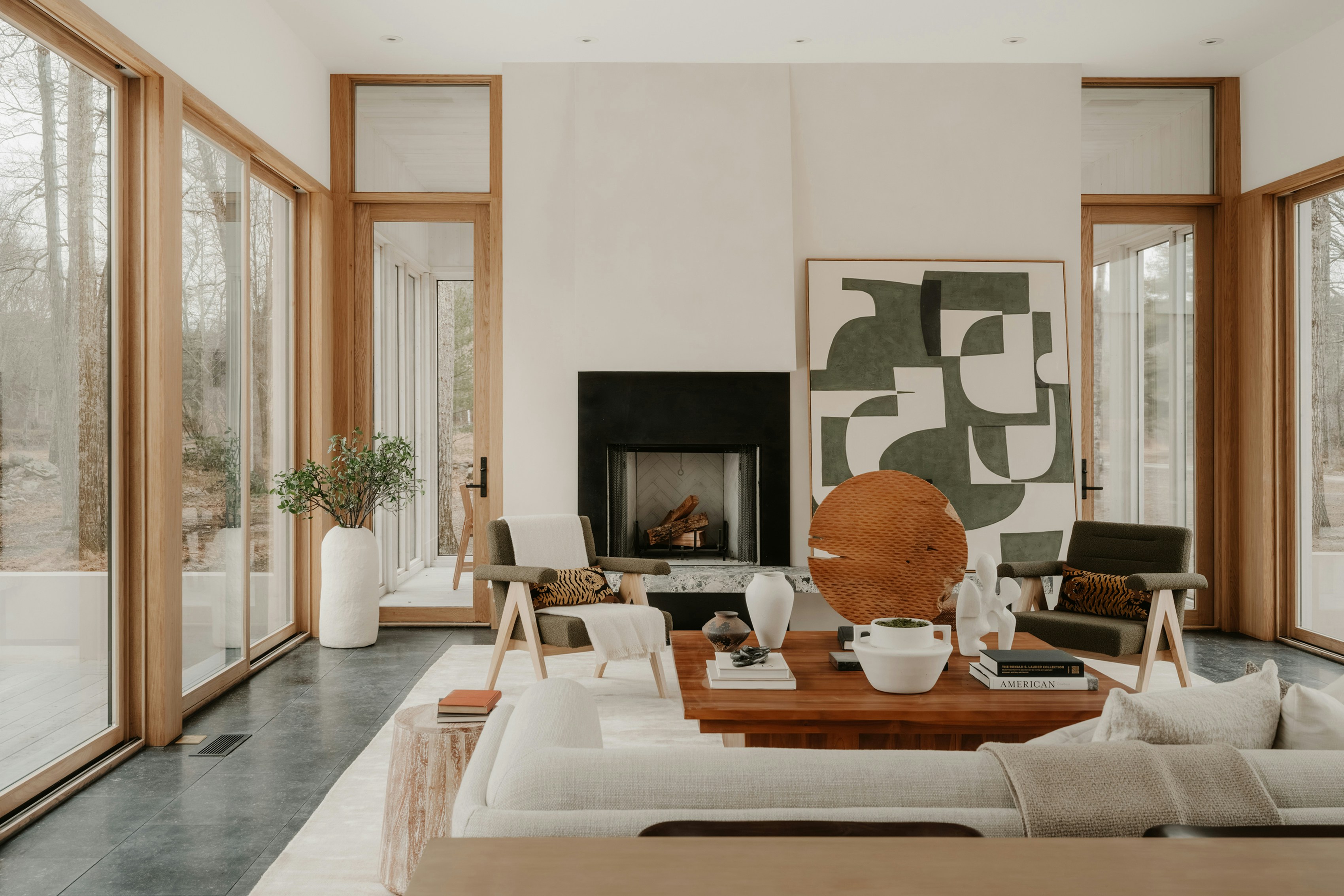 Contemporary forest retreat with oak-framed glass doors, stone fireplace, and oversized abstract artwork