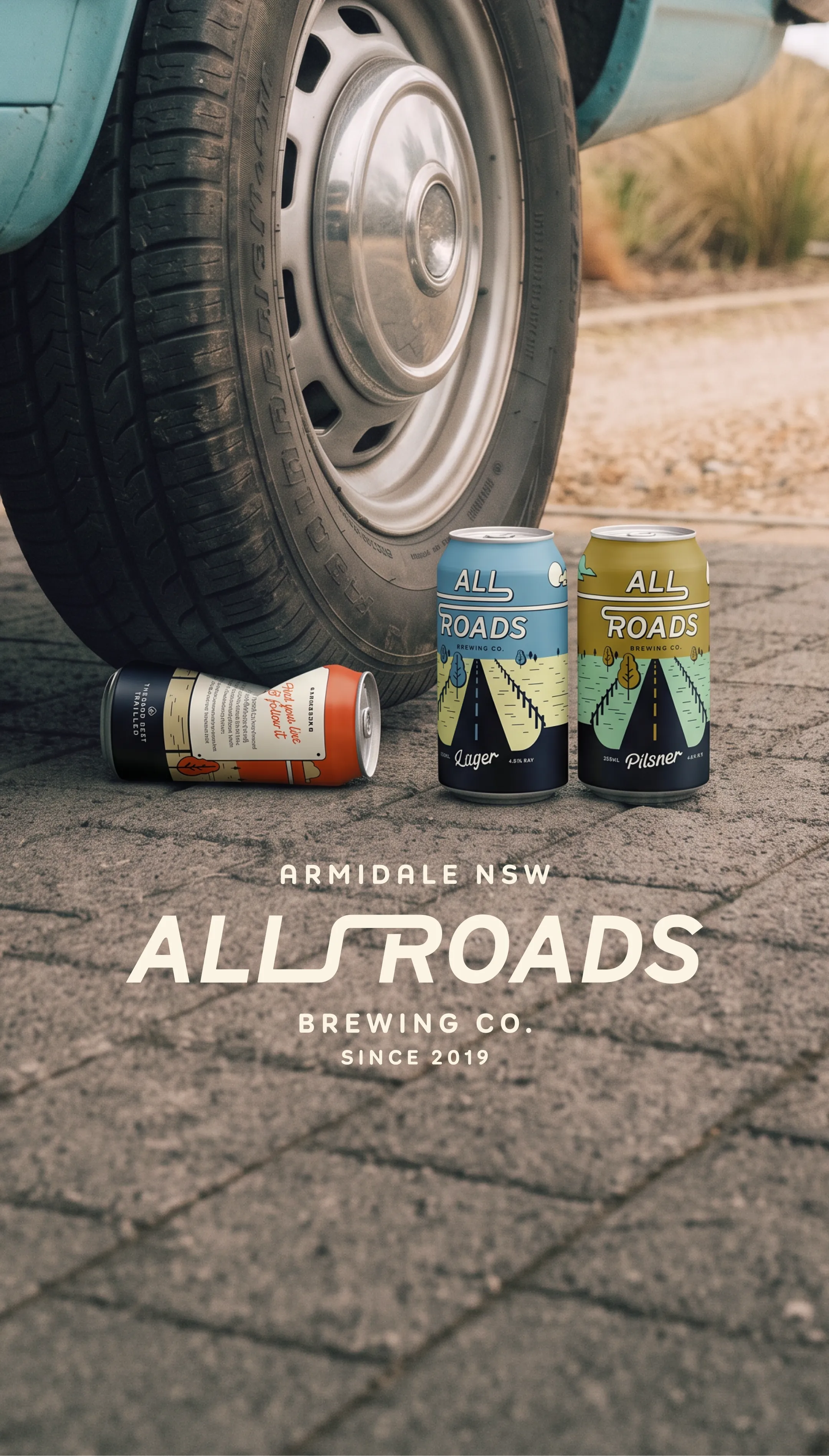 All Roads Brewing Co. brand photography showing cans on ground near vintage car wheel