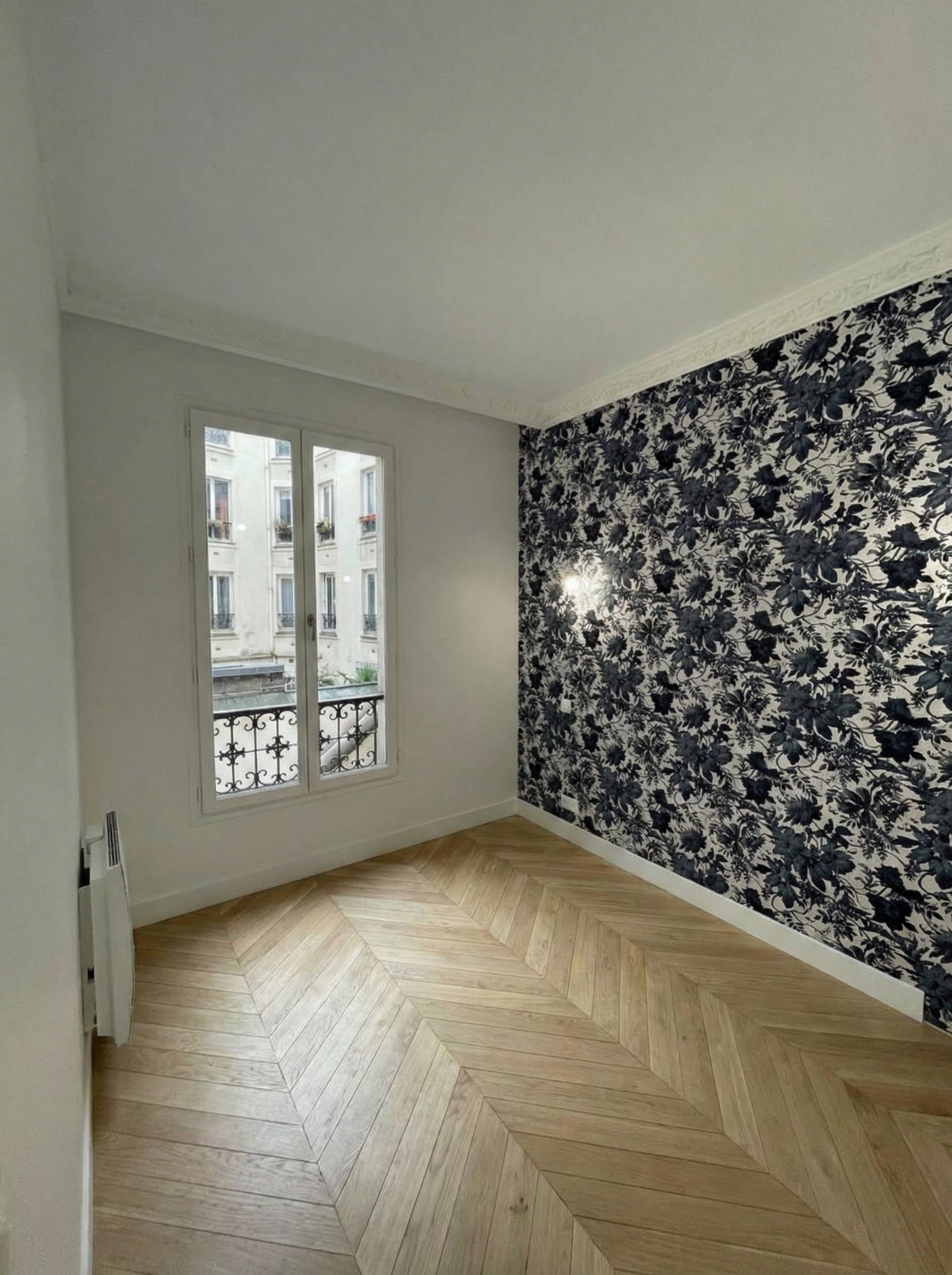 Décoration de chambre avec mur d'accent en papier peint floral bleu foncé et blanc contrastant avec le parquet ancien.