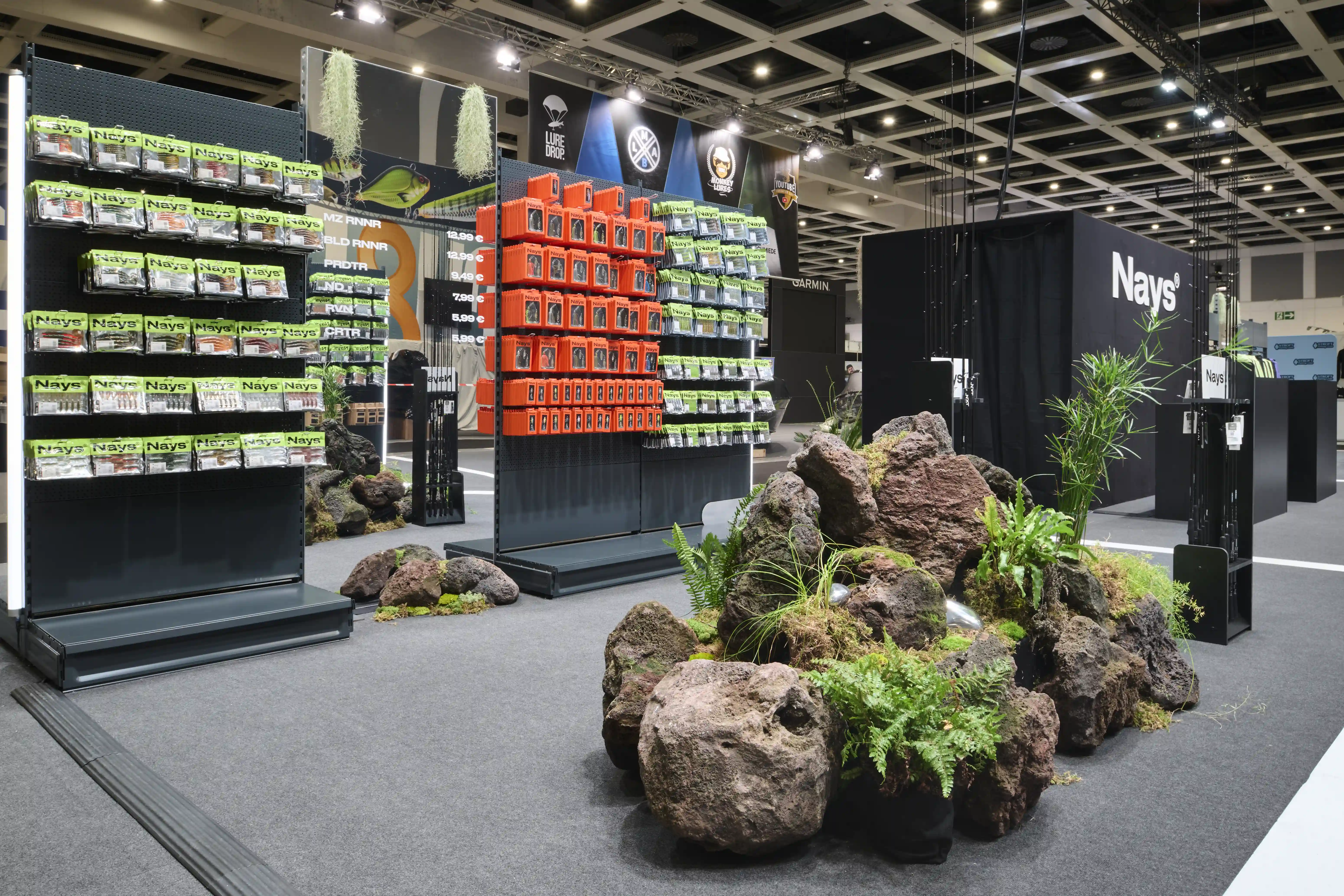 Display shelves with neon-green Nays packaging and orange boxes beside a large lava-rock planting at the booth.