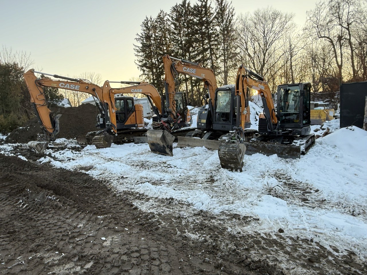 Four excavators lined up on a snowy jobsite at dusk, A&M Construction jobsite