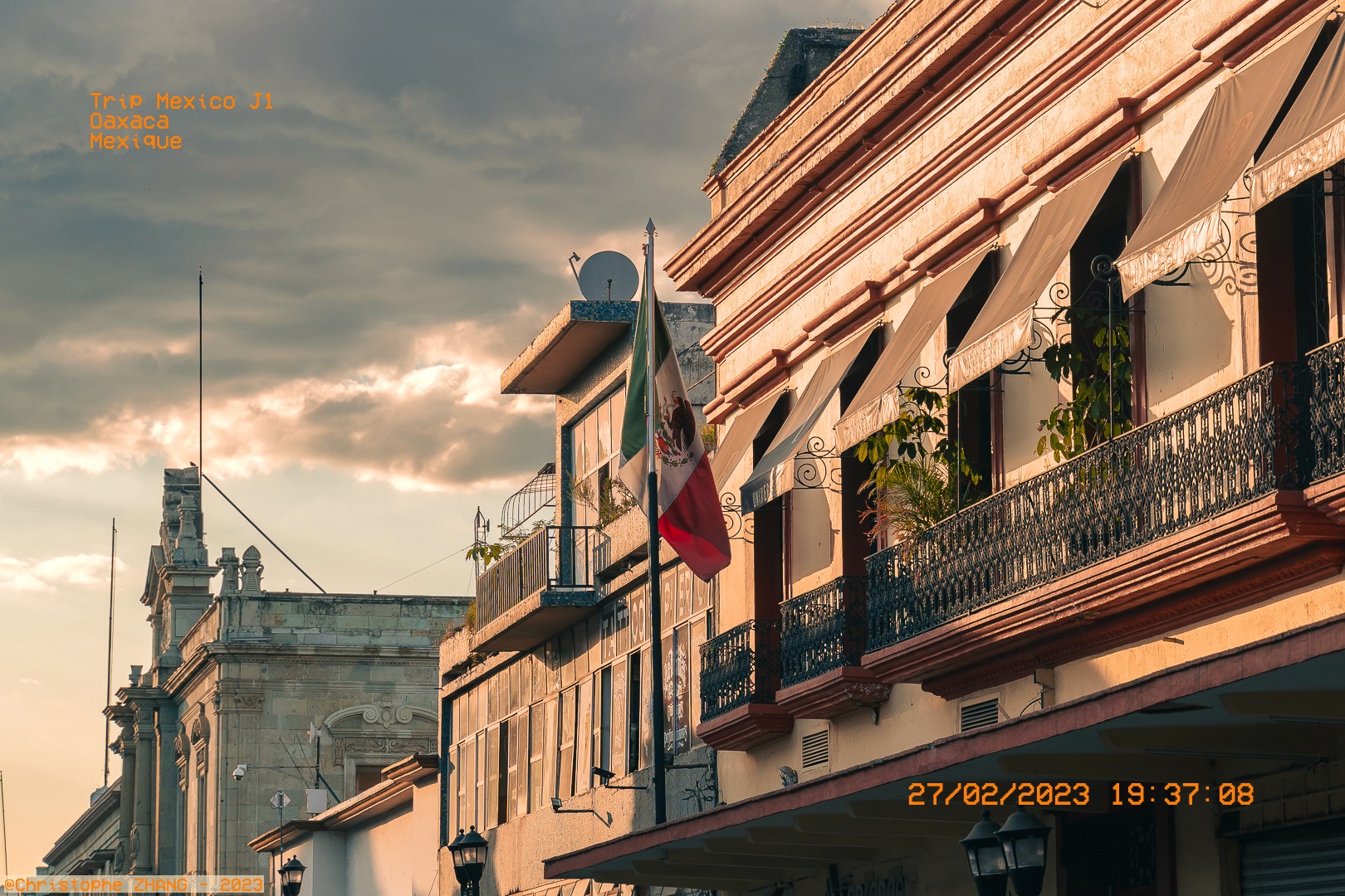 Façade d’un bâtiment colonial à Oaxaca avec un drapeau mexicain flottant au coucher du soleil.