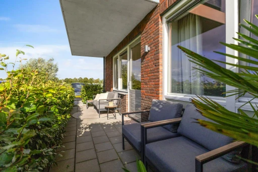 Het lange terras met loungemeubilair, planten en uitzicht op het groen.
