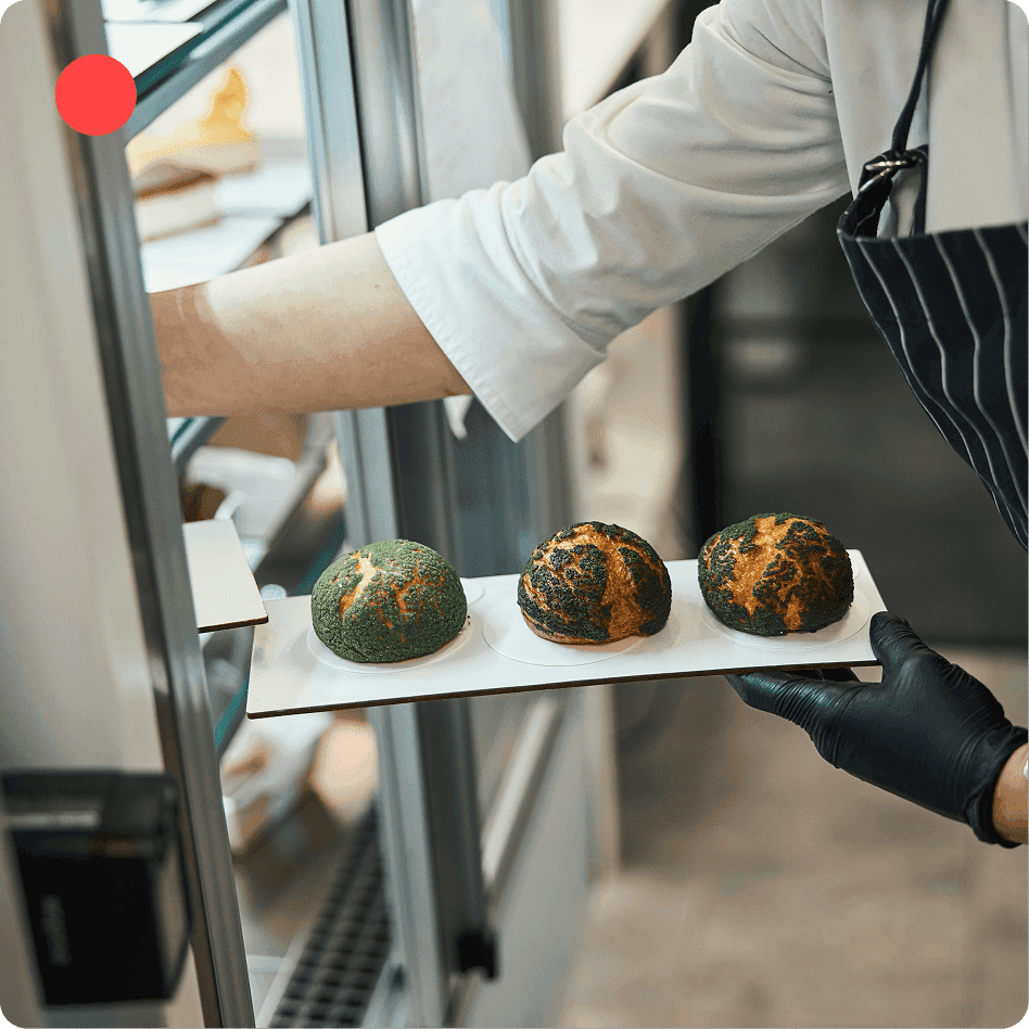 Person wearing gloves places a tray with decorated pastries into a refrigerator