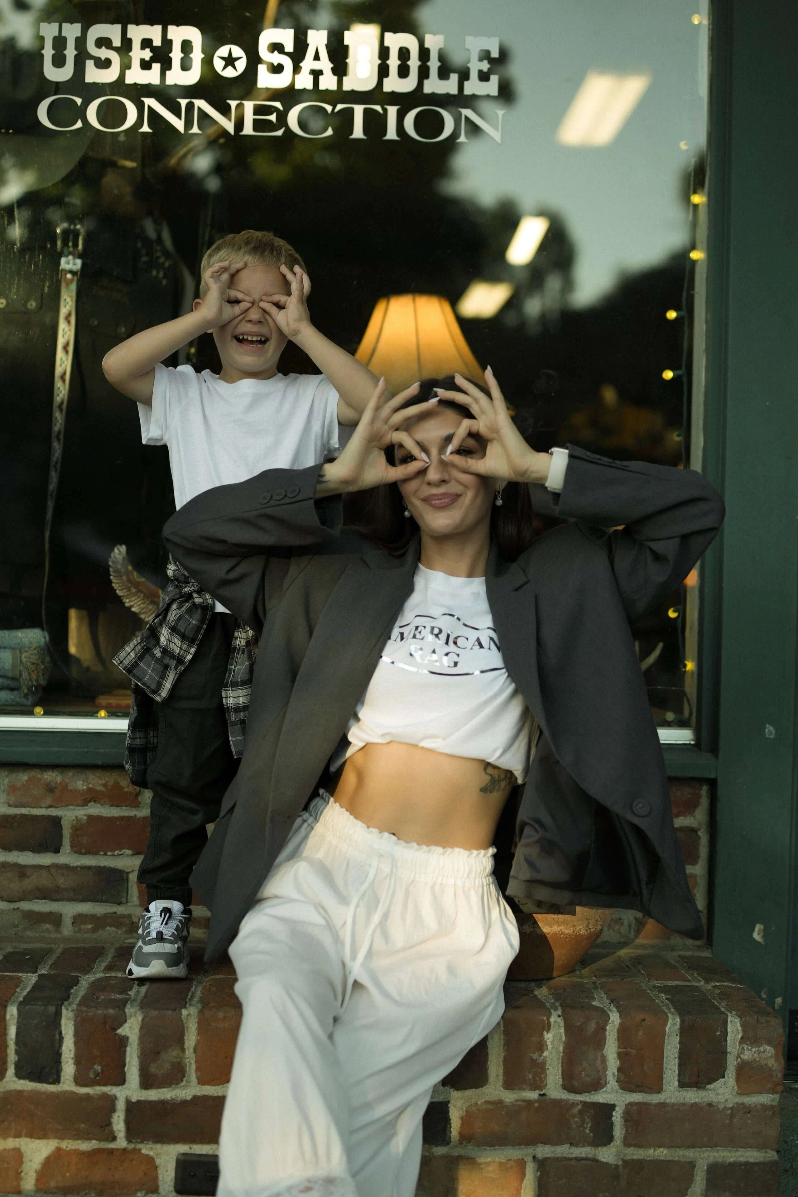 Mother and child making playful hand circles outside a storefront