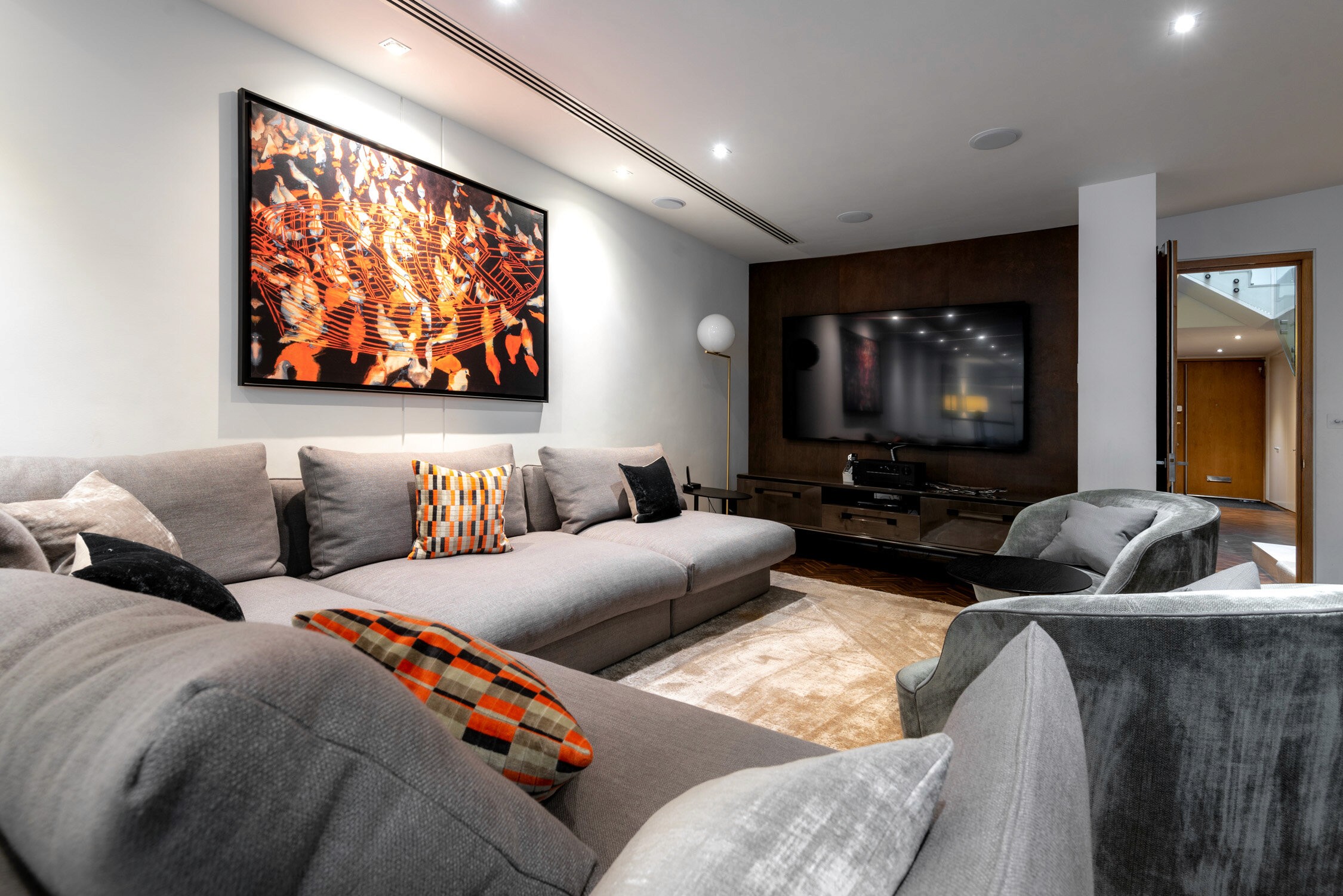 A modern living room features a large gray sectional sofa, a flat-screen TV on a dark wood console, and an abstract painting.